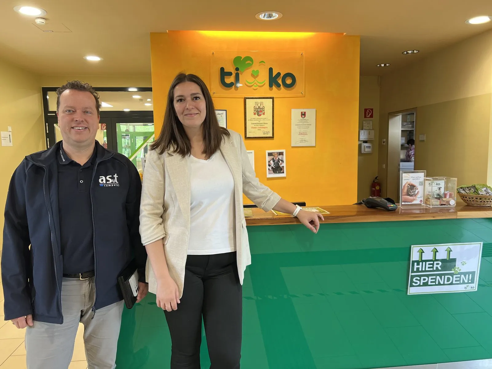 Kristina Koschier vom TIKO Tierheim Klagenfurt und ein asut-computer-Berater am Empfang unter dem TIKO-Logo
