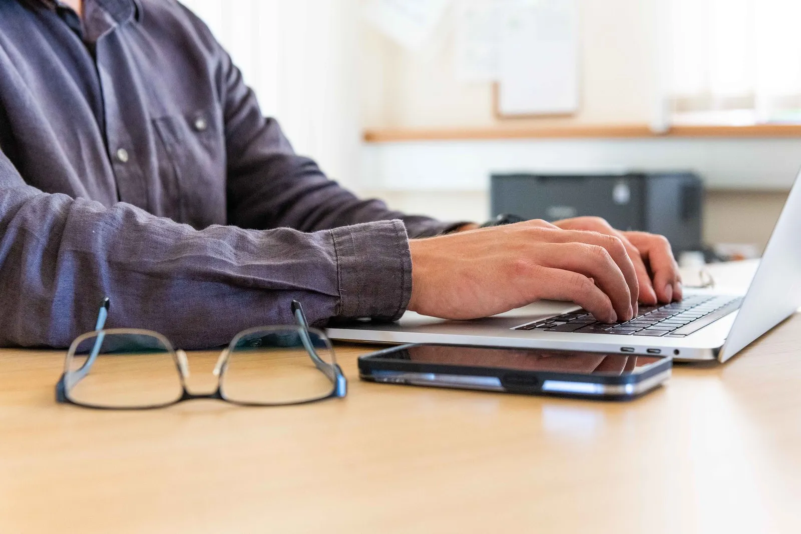 Hände tippen am Laptop neben Smartphone und Brille, Auswertung der Projektzeiten am Arbeitsplatz