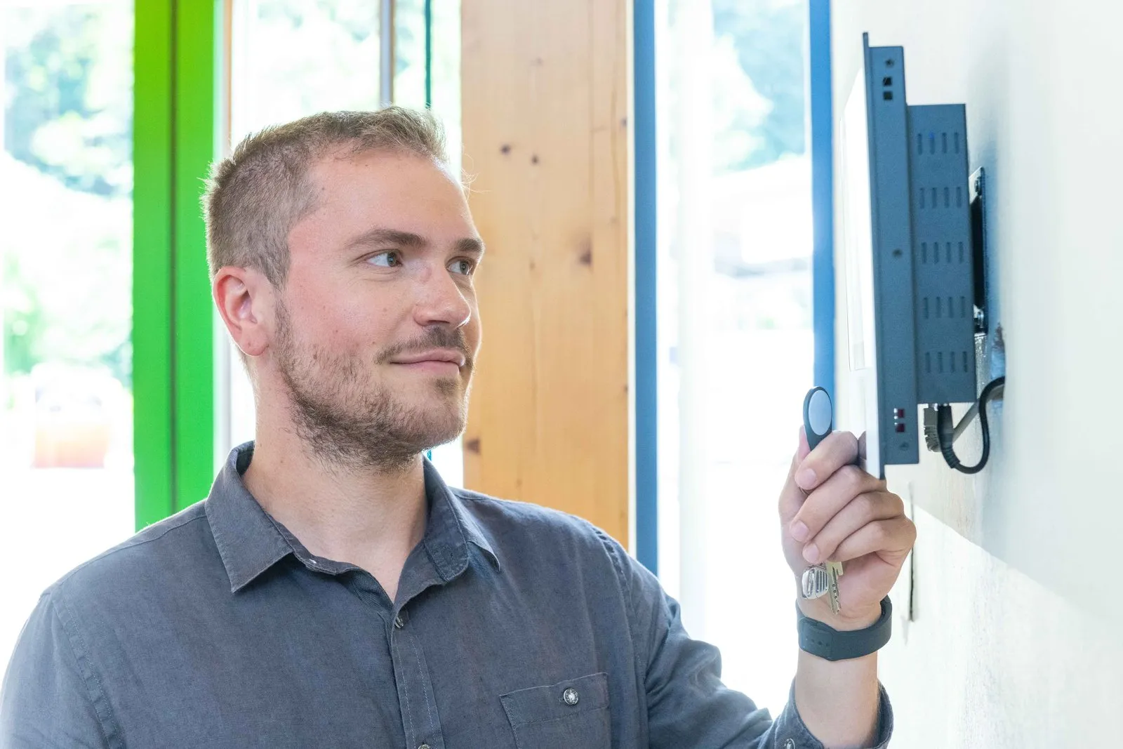 Mitarbeiter hält einen Transponder an ein Wand-Terminal zur Zutrittskontrolle im Eingangsbereich