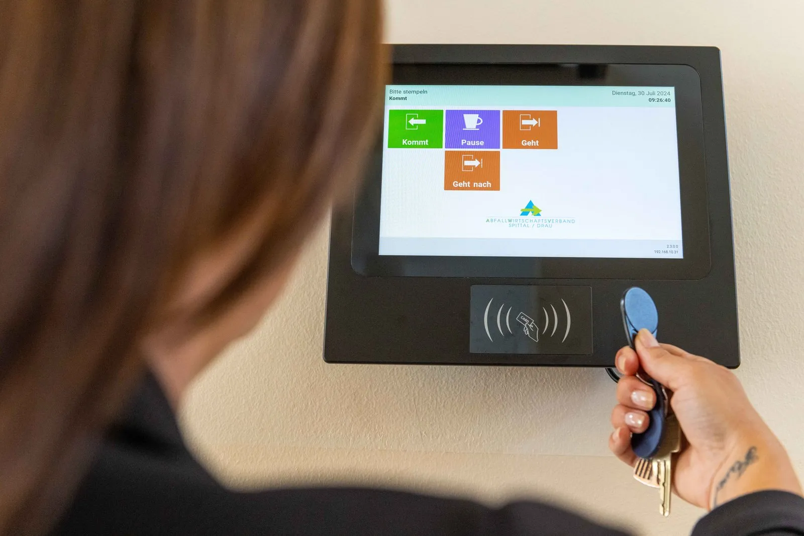 Timework Terminal mit Touch-Oberfläche und den Buttons Kommt, Pause und Geht, Mitarbeiterin stempelt am RFID-Leser