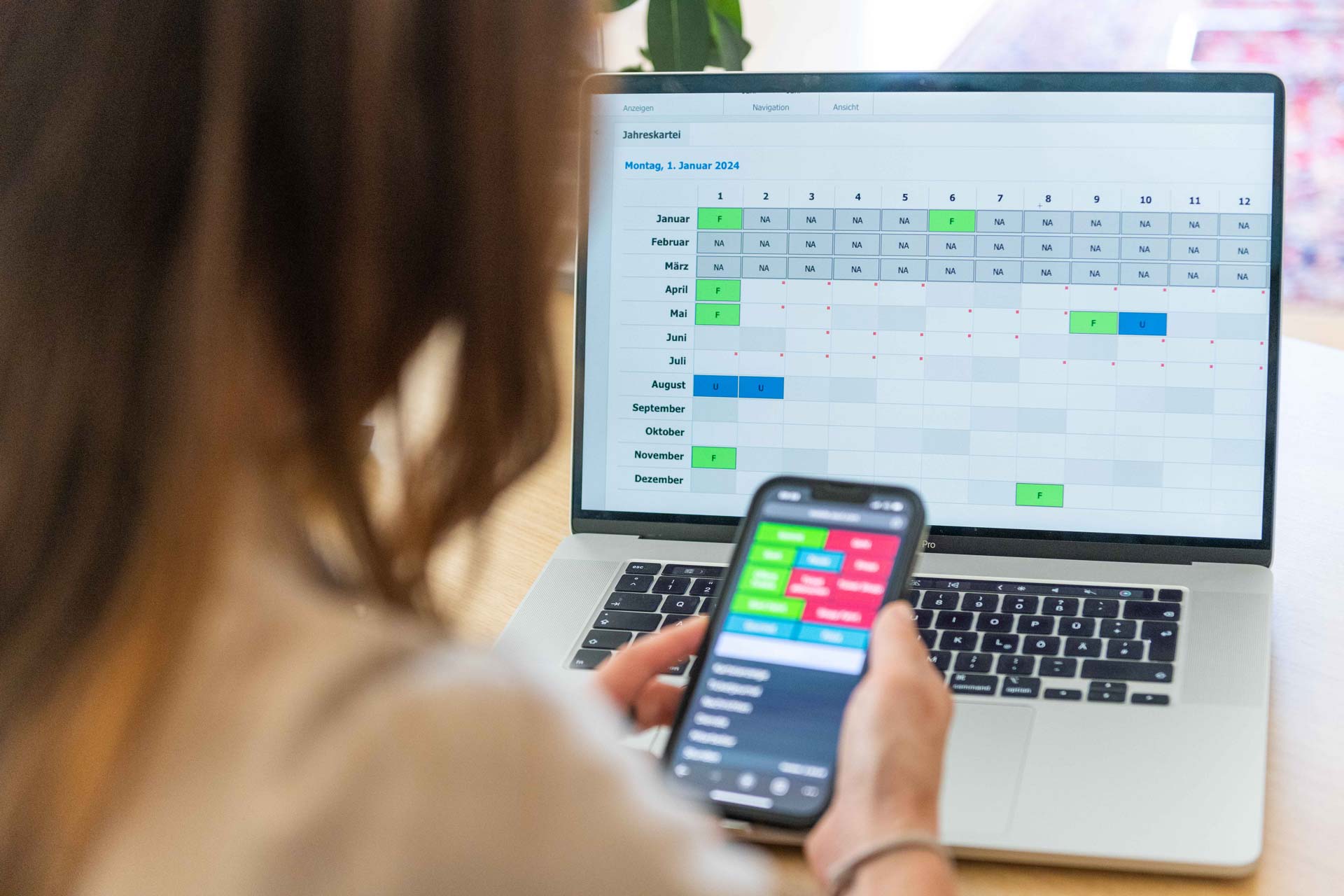 Frau sieht auf ihr Handy mit mobiler Zeiterfassung von asut computer, Laptop zeigt die Desktop-Version von Timework.