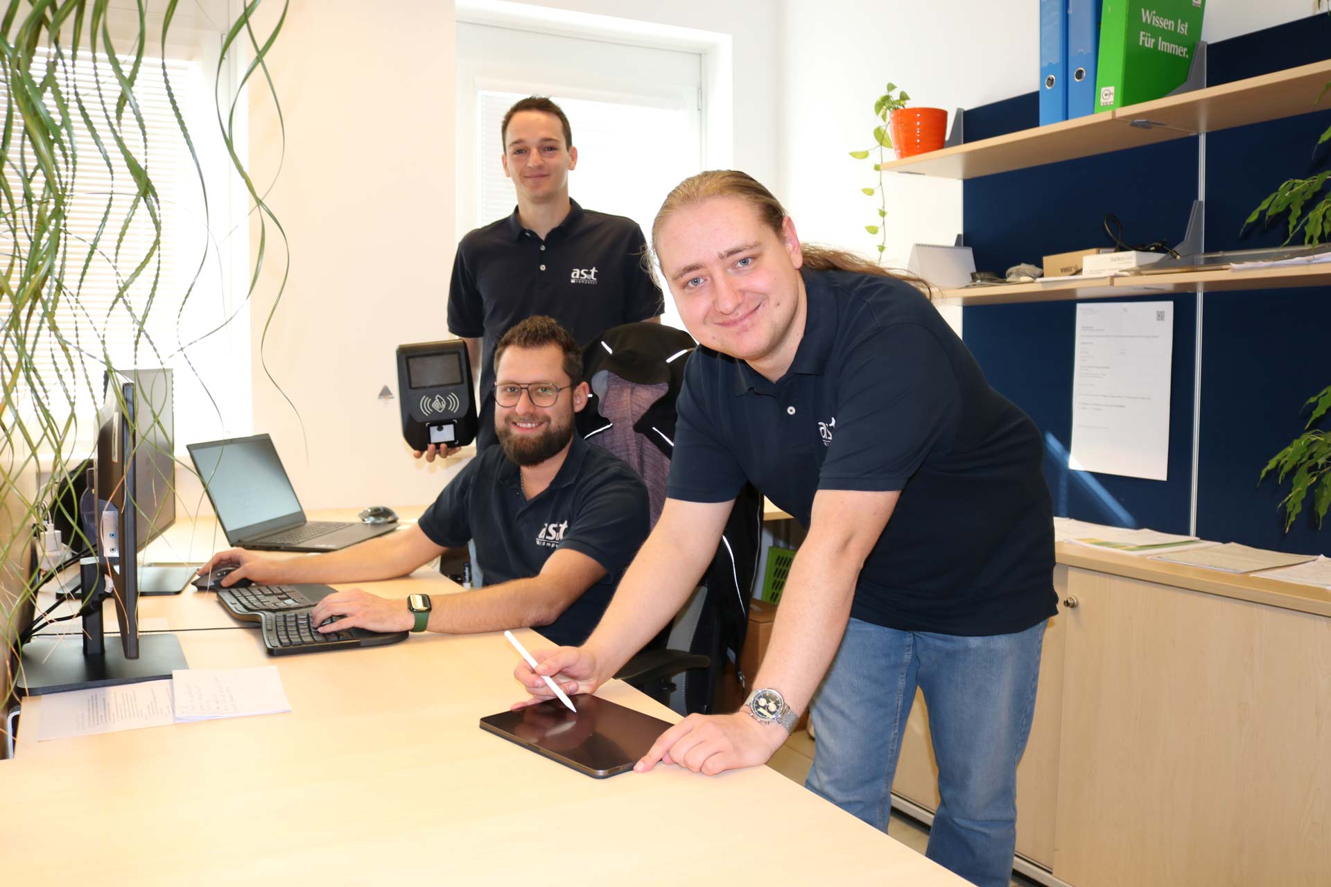 Drei Mitarbeiter der Zeiterfassung mit Tablet und Terminal vorm PC